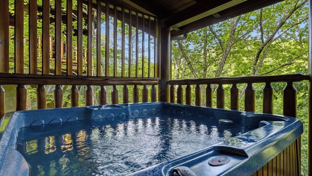 A hot tub with a wooden deck and railings, surrounded by trees. - Resort Location*15 minutes to Dollywood*Sleeps 10 (Pigeon Forge)