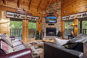 L’intérieur d’un chalet en bois est doté d’une cheminée, de canapés en cuir et d’un téléviseur fixé au-dessus de la cheminée.
