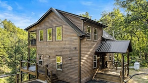 Eine zweistöckige Holzhütte mit Balkon, überdachter Veranda und kleiner Terrasse.