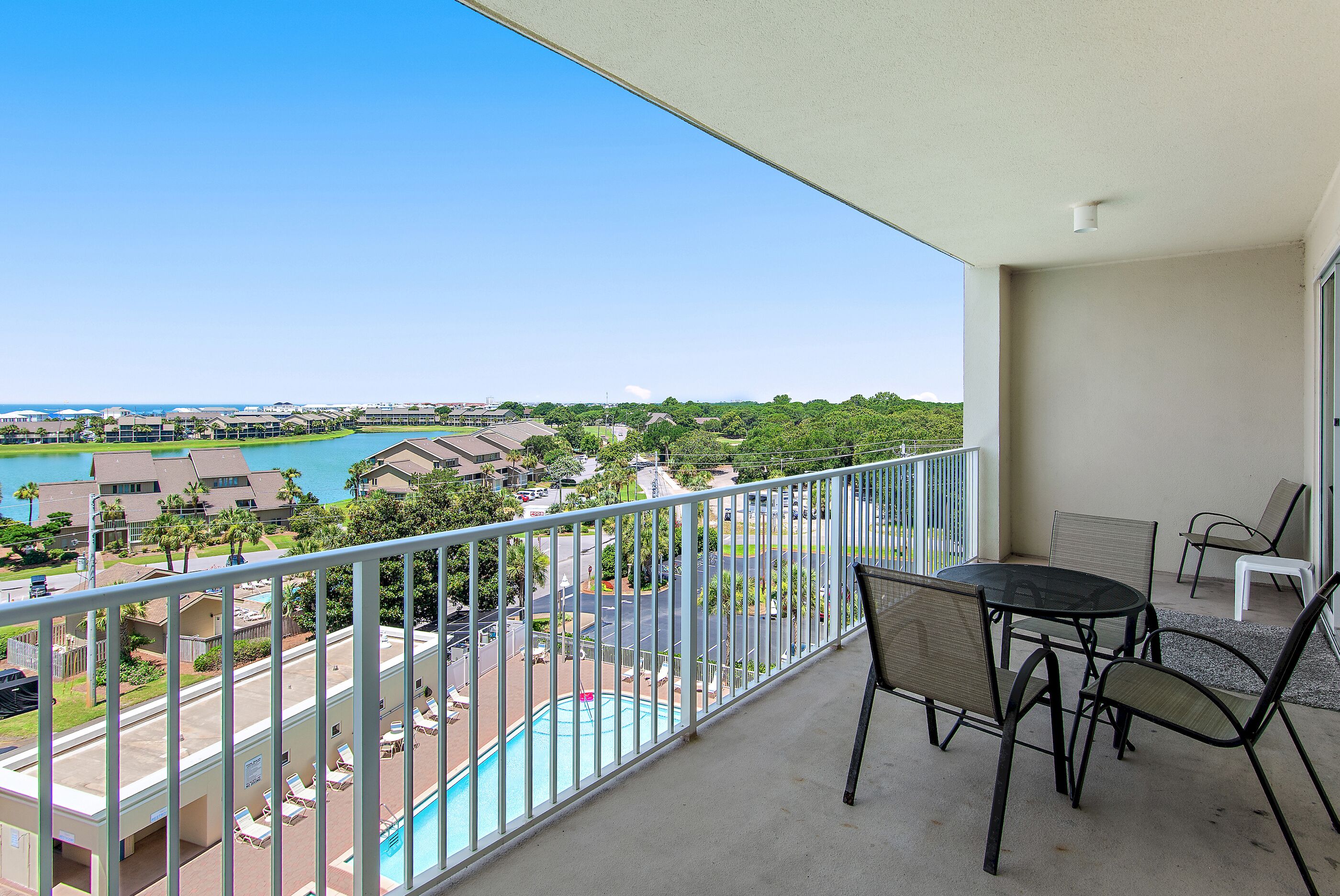 A balcony with a view of a swimming pool, lounge chairs, and a table.