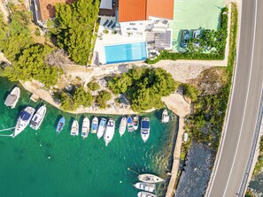 An aerial view of a coastal property with a swimming pool, multiple boats docked in the marina, and a road adjacent to the property. - Spacious Seafront Villa with Pool, Tennis, Gym & Mooring (Žaborić)