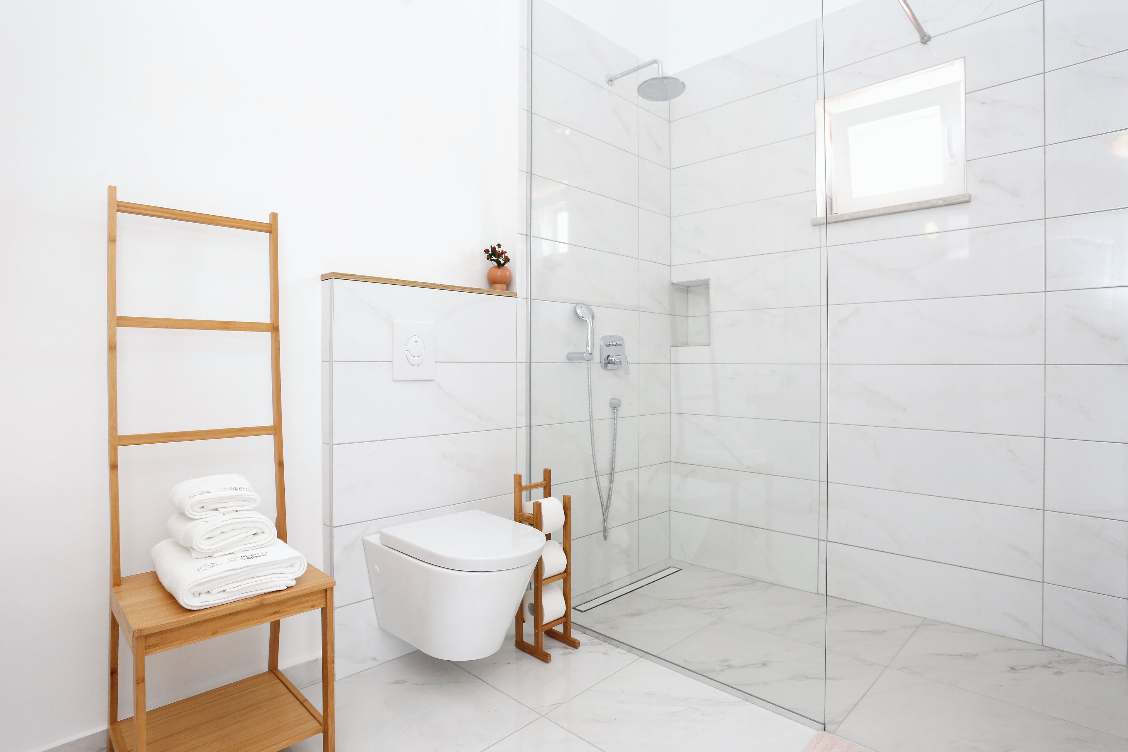 A modern bathroom with a toilet, a shower, and a wooden shelf with towels.