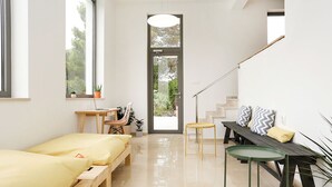 Ein modernes, helles Zimmer mit großem Fenster, einer hölzernen Bank, einem kleinen Tisch und einer Treppe.