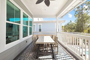 A covered patio with a wooden table and chairs, large windows, and a white railing. - New Listing Naturewalk: Private Heated Pool & Spa. EVCharger, Golf Cart & Bikes. (Santa Rosa Beach)