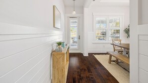 A hallway with white walls, a wooden bench, a dining table, and a hanging light fixture. - New Listing Naturewalk: Private Heated Pool & Spa. EVCharger, Golf Cart & Bikes. (Santa Rosa Beach)