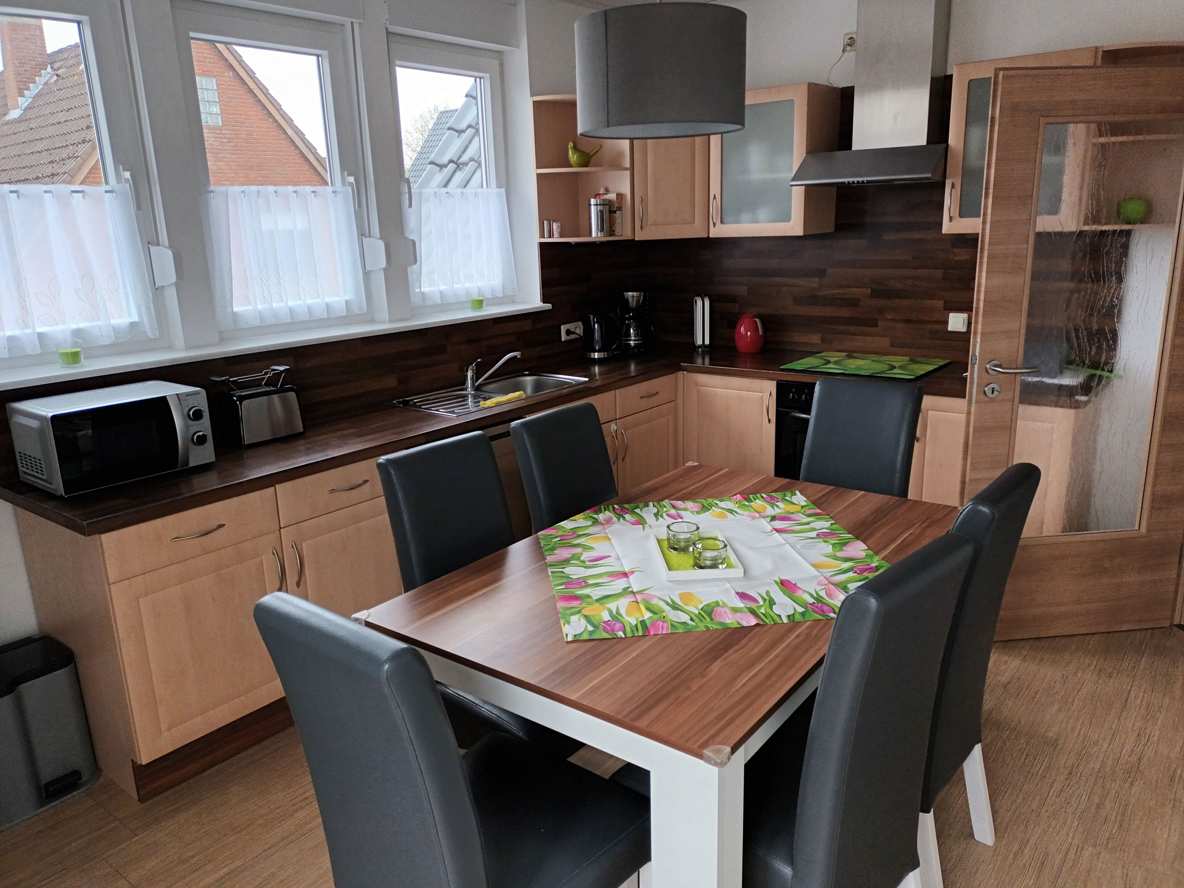 Een moderne keuken met houten kastjes, een eettafel met stoelen, een magnetron en een koffiezetapparaat.