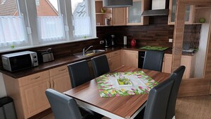 A modern kitchen with wooden cabinets, a dining table with chairs, a microwave, and a coffee maker. - Cozy vacation apartment with balcony. (Aschendorf)