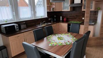 Een moderne keuken met houten kastjes, een eettafel met stoelen, een magnetron en een koffiezetapparaat.