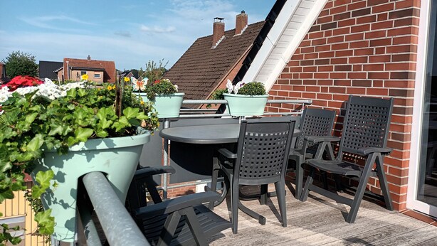 An outdoor patio with a table and chairs, surrounded by potted plants and a brick wall. - Cozy vacation apartment with balcony. (Aschendorf)