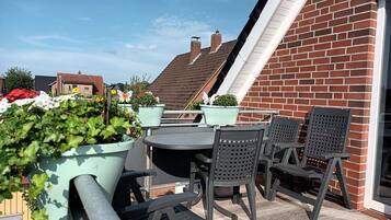 Een terras buiten met een tafel en stoelen, omringd door potplanten en een bakstenen muur.
