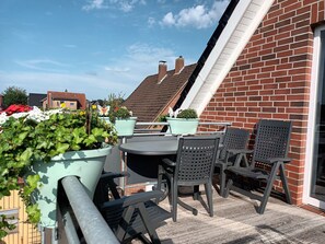 An outdoor patio with a table and chairs, surrounded by potted plants and a brick wall. - Cozy vacation apartment with balcony. (Aschendorf)