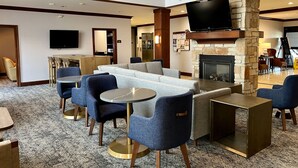 A hotel lobby with a stone fireplace, a flat-screen TV, a seating area with sofas and chairs, and a dining area with a table and chairs. - Accessible 1-BR Suite w/ Two Double Beds (Oconomowoc)