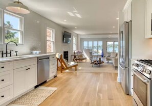 A modern kitchen with white cabinets, a built-in oven, and a large window overlooking a scenic view. - The Hamptons, Sag Harbor, Waterfront Escape (Sag Harbor)