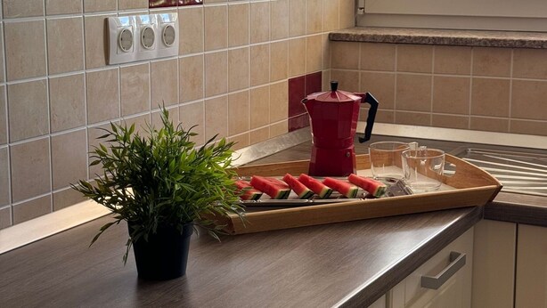 A kitchen with a wooden countertop, a potted plant, a cutting board with watermelon slices, and a red kettle. - Beautiful Apartment Bodulo 3 (Povljana)