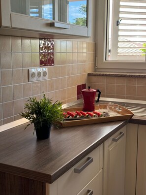 A kitchen with a wooden countertop, a potted plant, a cutting board with watermelon slices, and a red kettle. - Beautiful Apartment Bodulo 3 (Povljana)