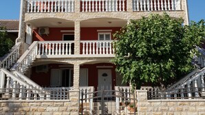 A multi-story building with a red facade, white balconies, and a stone entrance. - Beautiful Apartment Bodulo 3 (Povljana)