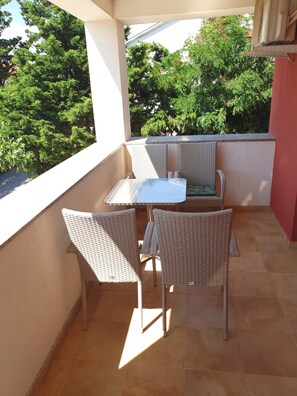 Ein Balkon mit Korbmöbeln, einem kleinen Tisch und Blick auf Bäume.