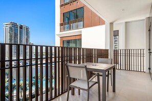 A balcony with a table and chairs, a view of a pool, and a high-rise building in the background. - Silkhaus Stylish 1bdr With Pool Balcony Dubai Creek Harbour (Dubai)