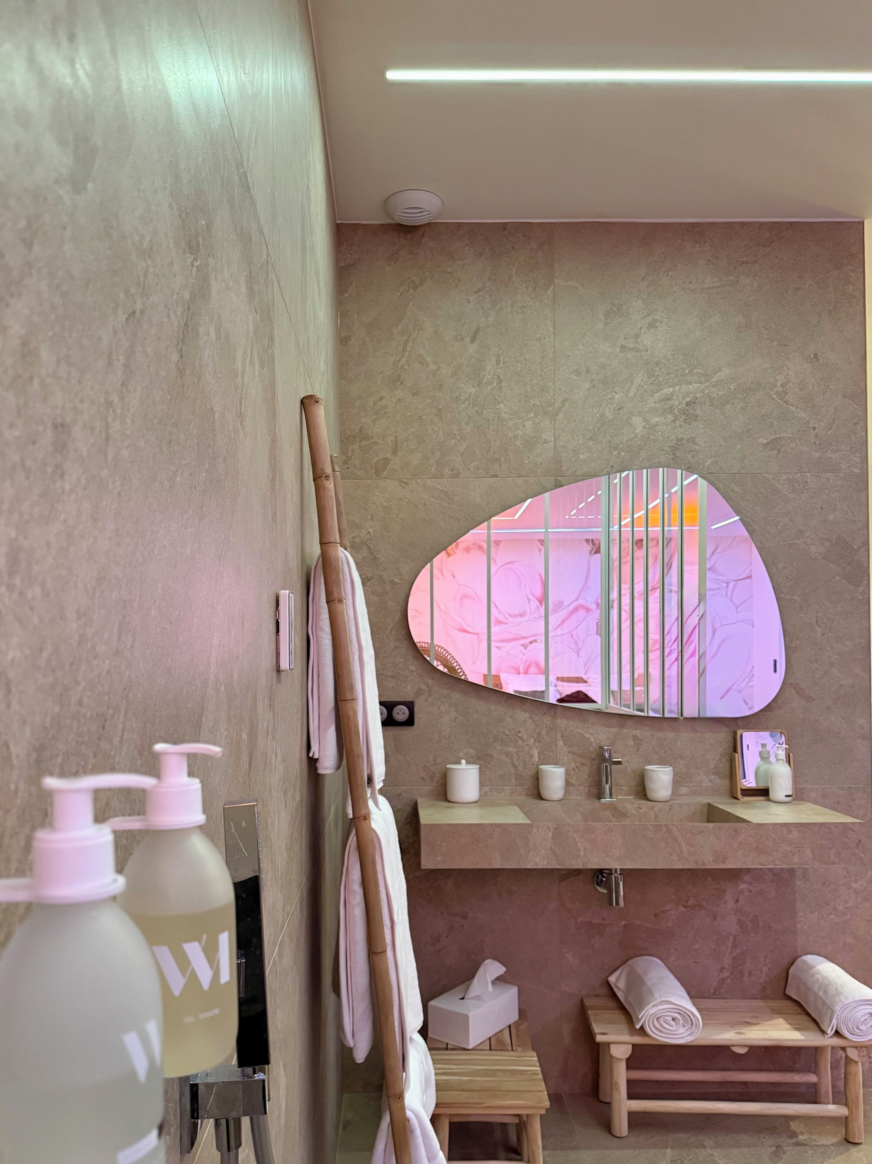Un baño moderno con un espejo grande, un banco de madera, un perchero y un tocador con espejo.