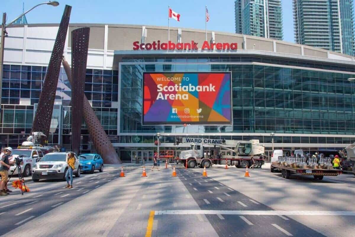 Exterior de l'Scotiabank Arena, amb un gran cartell de benvinguda, una façana moderna de vidre i una escultura metàl·lica característica.
