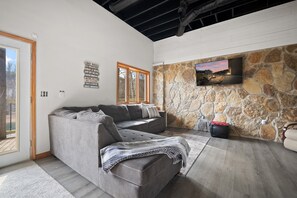 Un salon moderne avec un canapé d’angle, un mur en pierre et un téléviseur à écran plat fixé au mur.