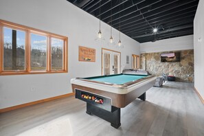 Une table de billard dans une pièce dotée de grandes fenêtres, un mur en pierre avec un téléviseur et un panneau indiquant un lieu de retraite.