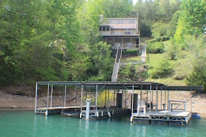A dock extending into a body of water with a house in the background surrounded by trees.