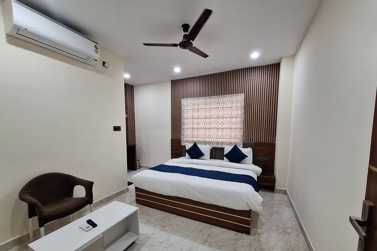 A bedroom with a bed, a chair, a TV stand, a ceiling fan, and a window with curtains.