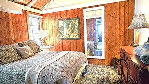 Een slaapkamer met houten lambrisering, een bed, nachtkastje, lamp en een kledingkast.