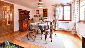 A dining area with a table, chairs, a chandelier, a wooden cabinet, and a window with curtains. - Gîte Vigne en fleur (Ribeauvillé)