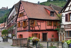 Ein traditionelles Fachwerkhäuschen mit einem steilen Satteldach, einem kleinen Balkon mit Blumen und einer Steinmauer davor.