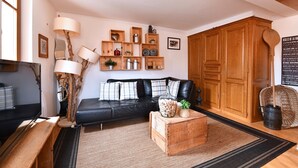A living room with a black leather sofa, wooden shelves with various items, a wooden coffee table, and a large wooden wardrobe. - Gîte Vigne en fleur (Ribeauvillé)
