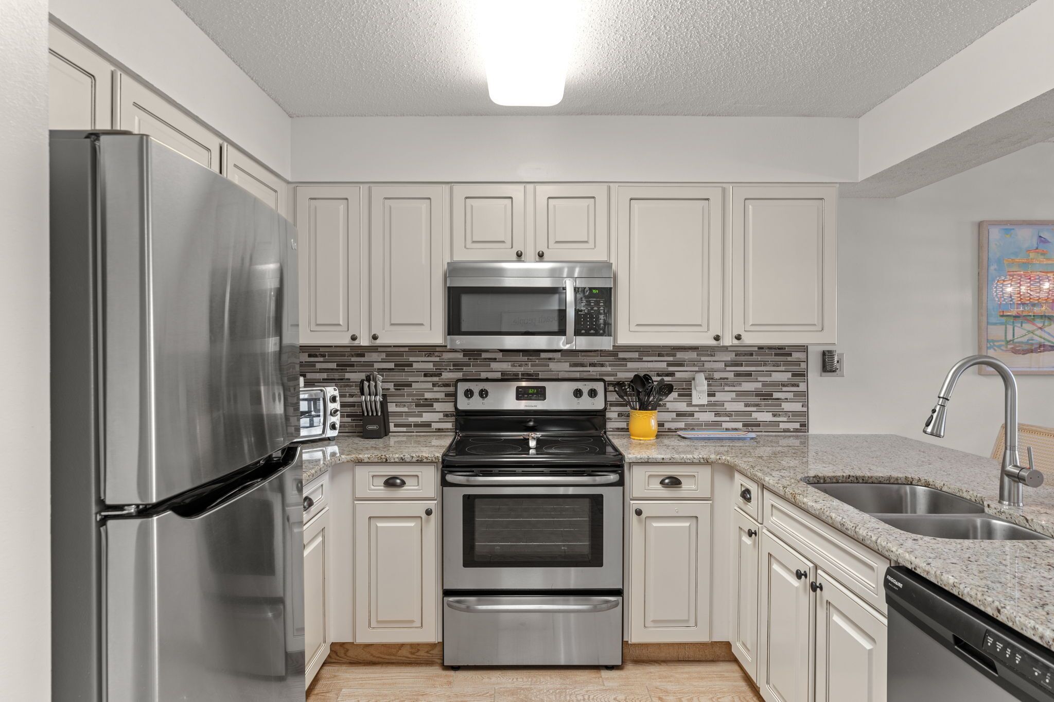 A modern kitchen with stainless steel appliances, white cabinets, a tiled backsplash, and a built-in dishwasher.