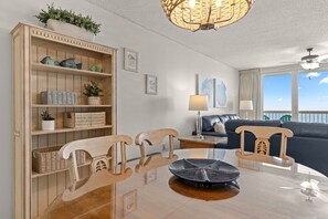A modern living room with a glass dining table, wooden chairs, a sofa, and a ceiling fan. - Stunning Gulf Views, Multiple pools, Perfect blend of relaxation and convenience (Destin)