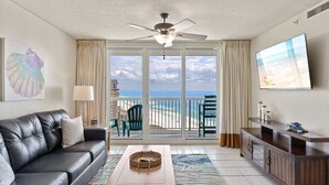 Ein Wohnzimmer mit Ledersofa, Couchtisch aus Holz, Fernseher und Blick auf den Strand durch große Schiebetüren.