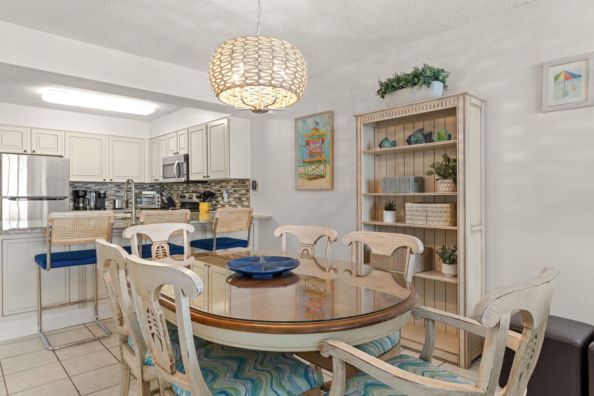 A modern kitchen with white cabinets, a stainless steel refrigerator, and a dining area with a glass table and wicker chairs.