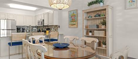A modern kitchen with white cabinets, a stainless steel refrigerator, and a dining area with a glass table and wicker chairs.