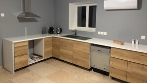 Une cuisine moderne avec un plan de travail blanc, des armoires en bois, un lave-vaisselle encastré, une fenêtre et un appareil de climatisation.