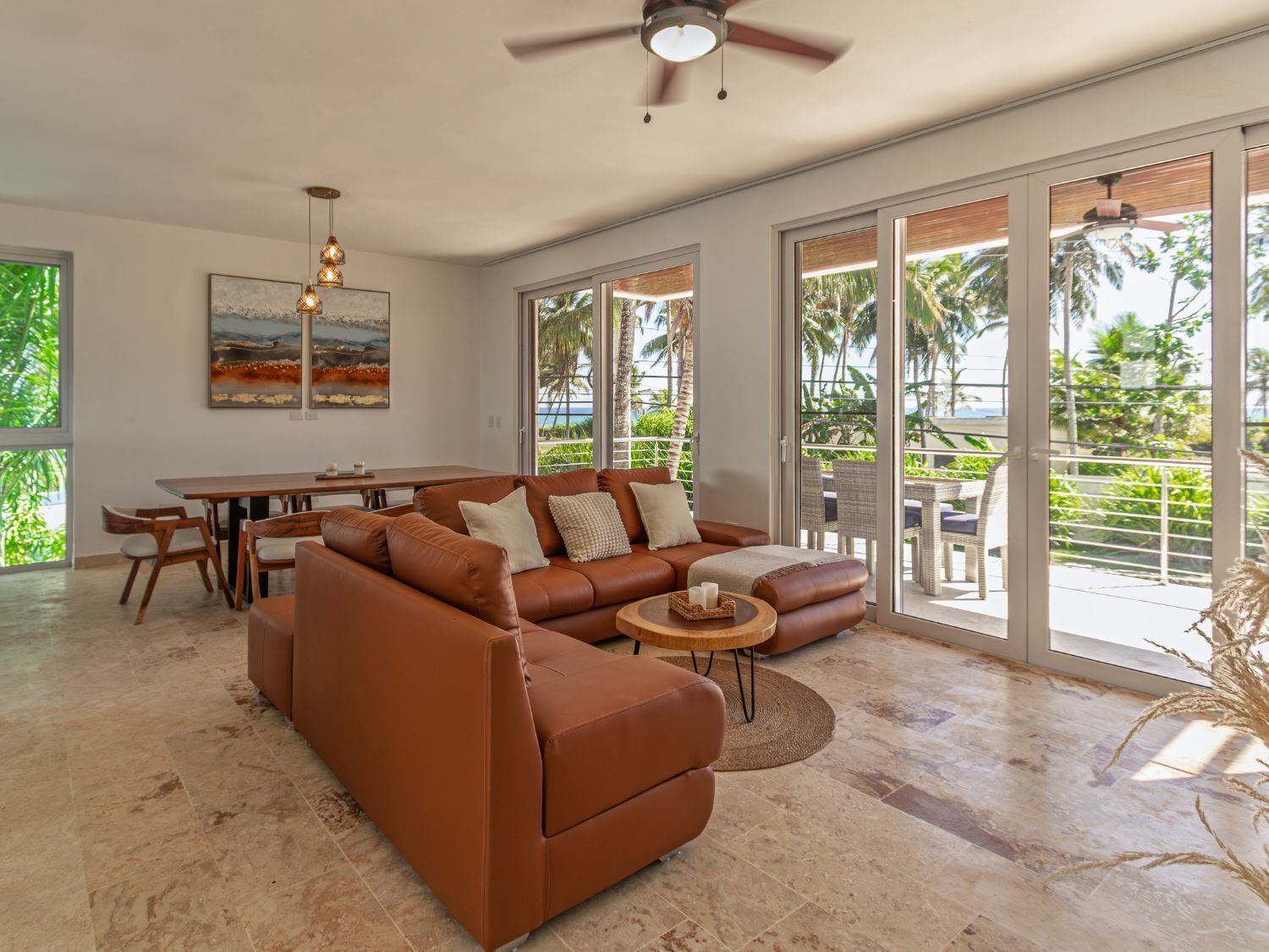 A spacious living area with a brown leather sofa, a dining table, and a ceiling fan.