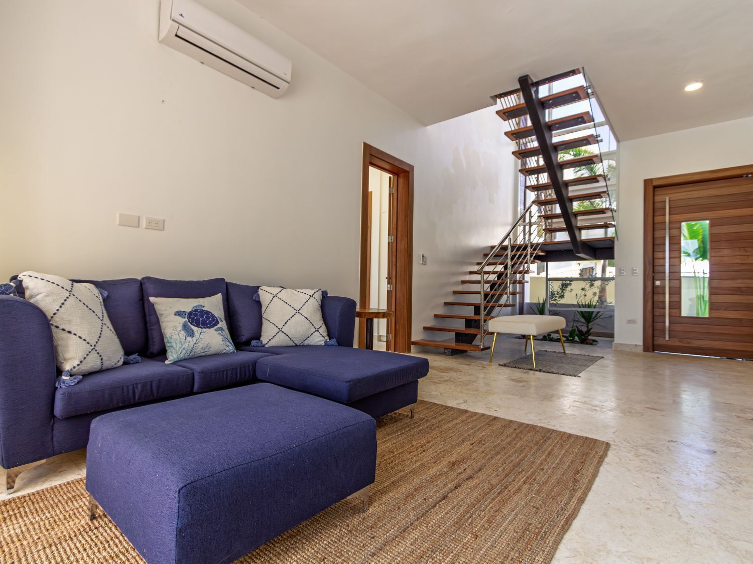 A modern living room with a sectional sofa, a staircase, and a view of the outdoors.