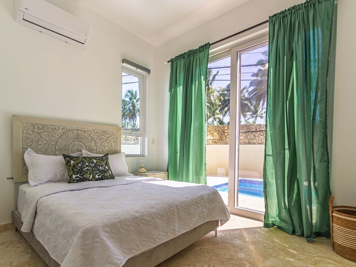 Un dormitorio con cama, mesita de noche, lámpara y vistas a una piscina a través de un ventanal corredera.
