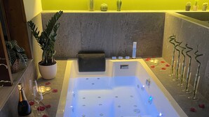 Ein moderner Spa-Bereich mit einer großen, beleuchteten Whirlwanne, einer Topfpflanze und einer Champagnerflasche auf der Ablagefläche.