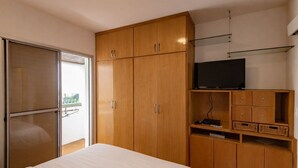A bedroom with a bed, wooden wardrobe, TV, and a balcony with a view. - Apto com Piscina e Garagem Perto do Ibirapuera (São Paulo)