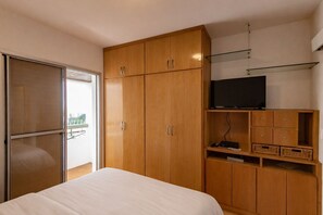 Ein Schlafzimmer mit Bett, Holzschrank, Fernseher und einem Balkon mit Aussicht.