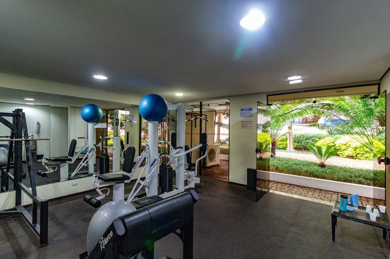Ein Fitnessraum mit Trainingsgeräten, einer Bank und Blick auf einen Garten.