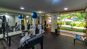 A gym with exercise equipment, a bench, and a view of a garden. - Apto com Piscina e Garagem Perto do Ibirapuera (São Paulo)