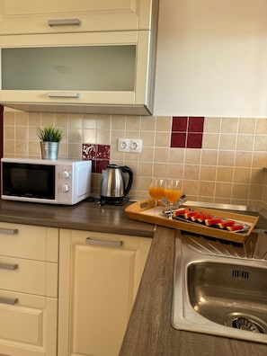 A kitchen with a microwave, kettle, and a tray with sliced fruit and glasses of orange juice. - Beautiful Apartment Bodulo 4 (Povljana)