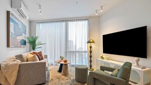 A modern living room with a sofa, armchair, coffee table, floor lamp, and a TV mounted on the wall. - Skyline Suite Southbank. Spectacular Views, Heated Pool, Gym, Sauna + (Southbank)