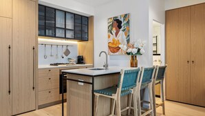 A modern kitchen with wooden cabinets, a central island, bar stools, and a painting above the sink. - Skyline Suite Southbank. Spectacular Views, Heated Pool, Gym, Sauna + (Southbank)