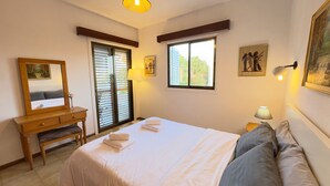 Un dormitorio con cama, escritorio, silla, ventana y puerta con persianas.